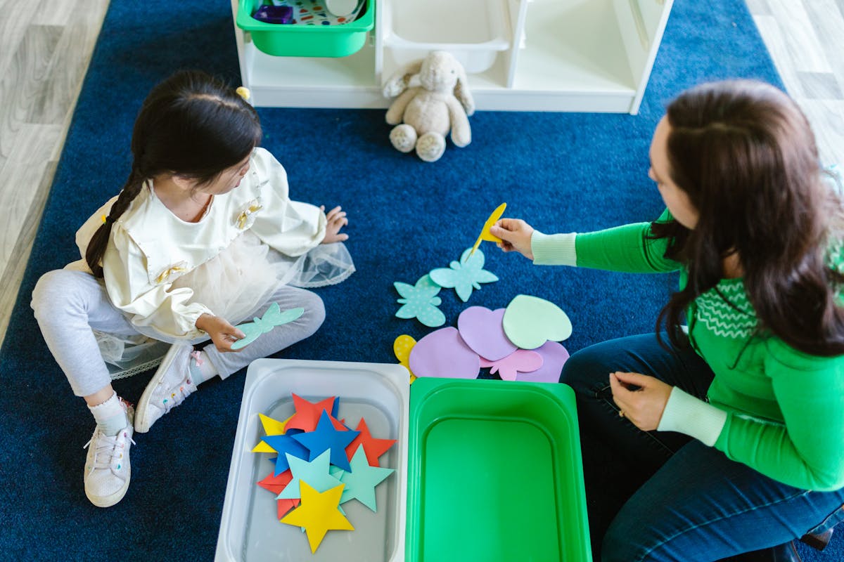Child learning with colourful shapes alongside a teacher